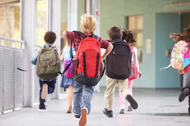 Niños corriendo por el pasillo de un centro escolar con mochilas a las espaldas.