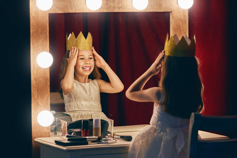 A young girl places a crown on her head while looking in the mirror.