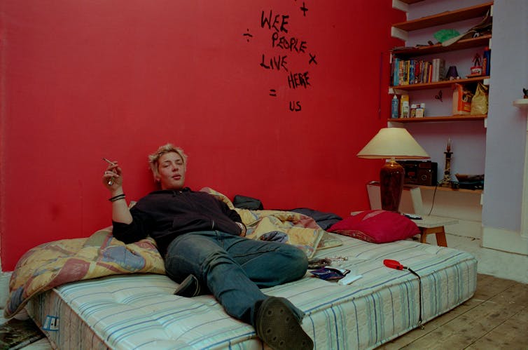 A girl smokes on a mattress in a squat