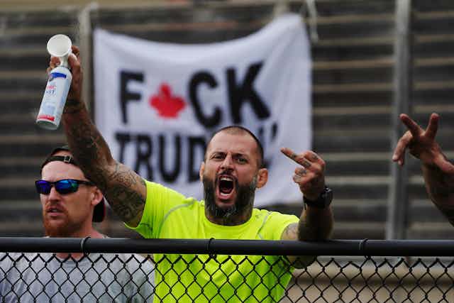 A man raises his middle finger as he stands in front of a sign disparaging Trudeau.