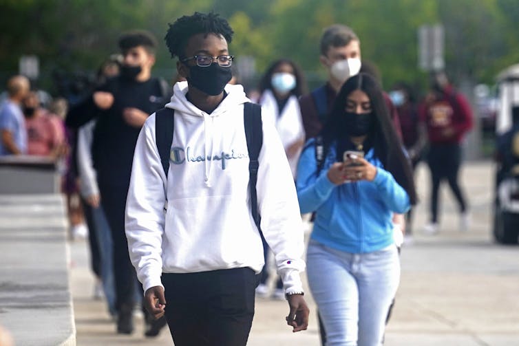 Students wearing face masks walk to school on the street.