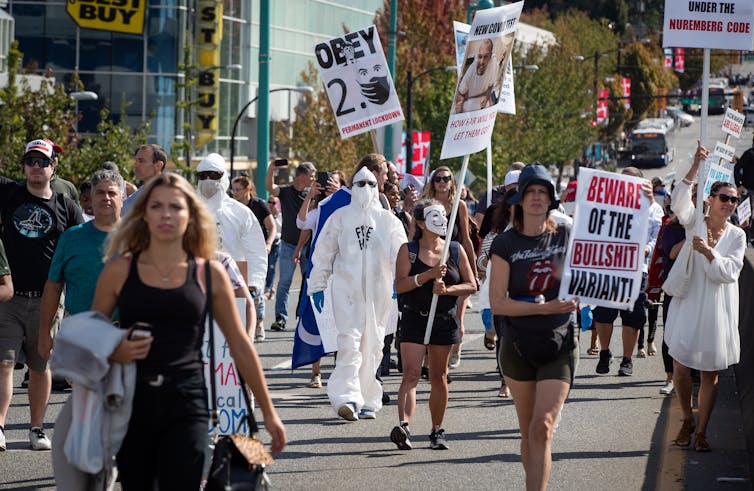 Protesters hold signs that read 'beware of the bullshit variant' at a protest for vaccinations/vaccine passports
