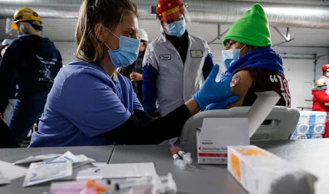 A Tyson Foods employee with a green hat receives a covid-19 shot during a workplace vaccination event