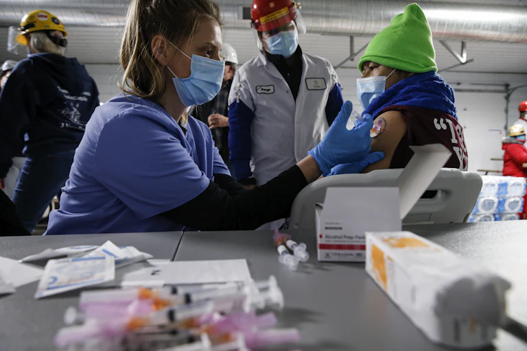 A Tyson Foods employee with a green hat receives a covid-19 shot during a workplace vaccination event