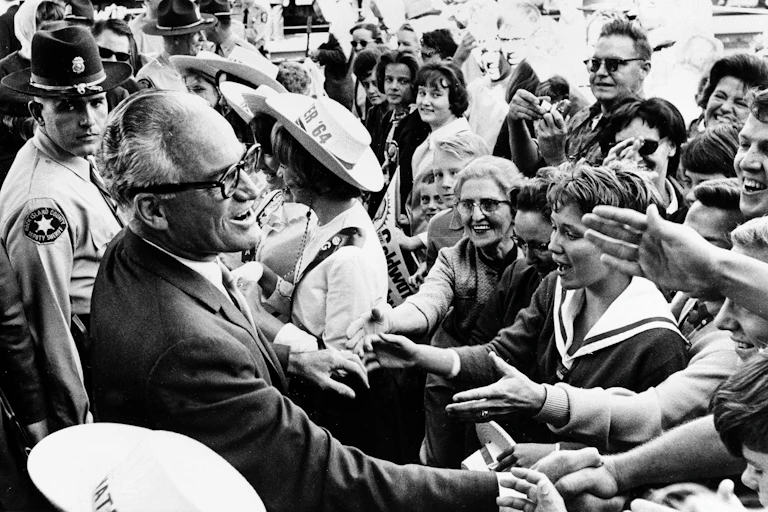 A black and white image of a man smiling and shaking hands with a crowd of people