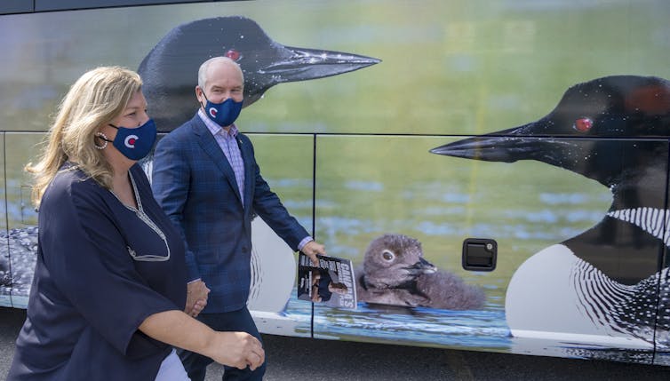 O'Toole and his wife walk past a mural on his campaign bus that shows loons.