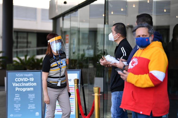 People in masks stand waiting outside a vaccination hub.