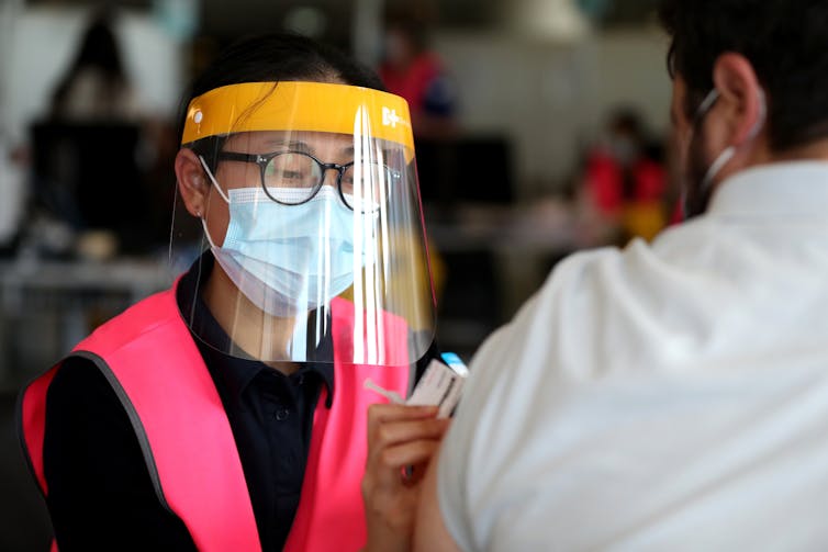 Vaccinator in a pink vest injects a vaccine into a man's arm.