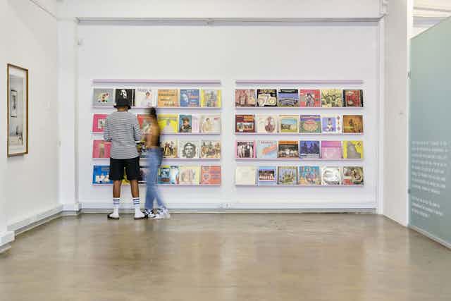 Two people stand looking at shelves covering a wall and containing colourful vinyl records.