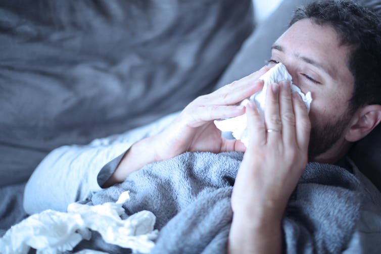 A man suffering a breakthrough infection, blowing his nose