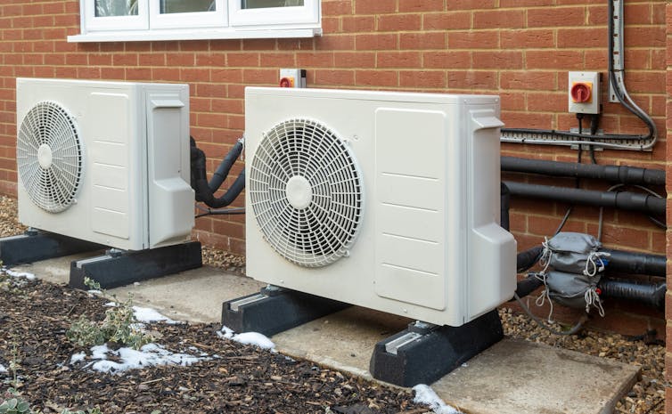 Two heat pump units with large fans installed on the outside of a house.