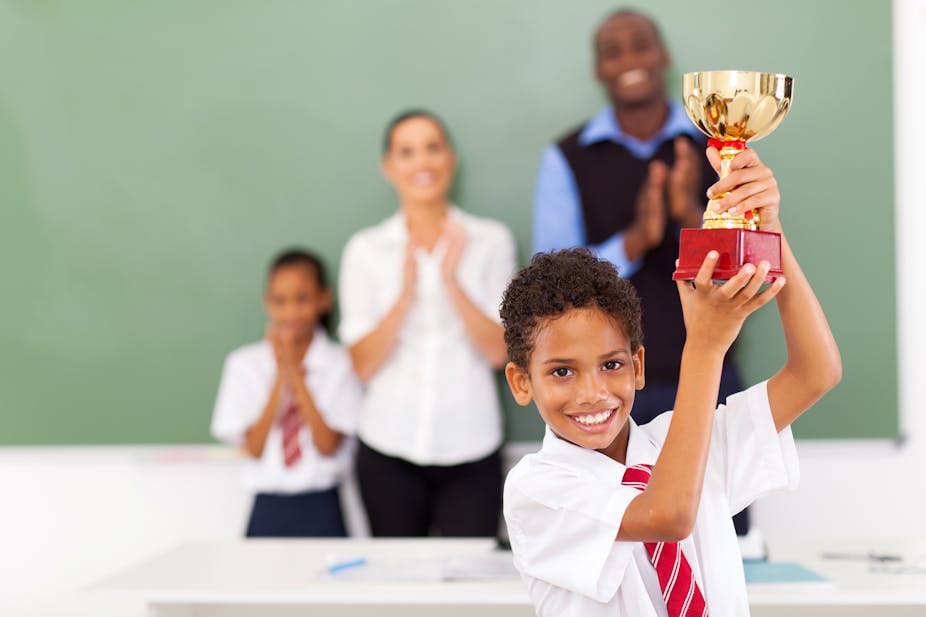 A young school boy holding a trophy in a classroom.