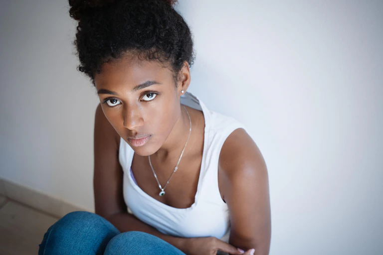 A young girl sits on the floor holding her stomach and looking anxious