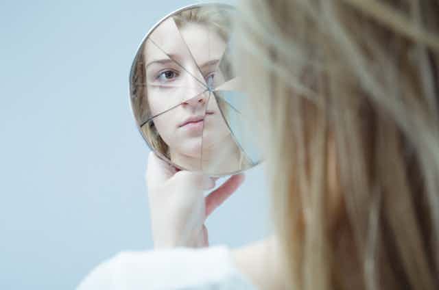 Una mujer se refleja en un espejo roto.