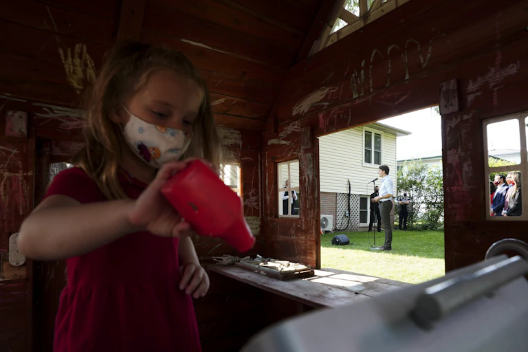 A girl plays house with Justin Trudeau seen talking into a microphone behind her.
