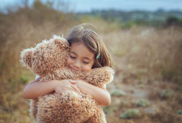 Young girl hugs brown teddy bear