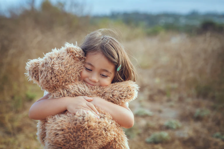 Young girl hugs brown teddy bear