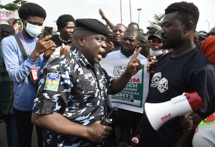 A man wearing a police uniform talks and points towards a man in black t-shirt, holding a megaphone.