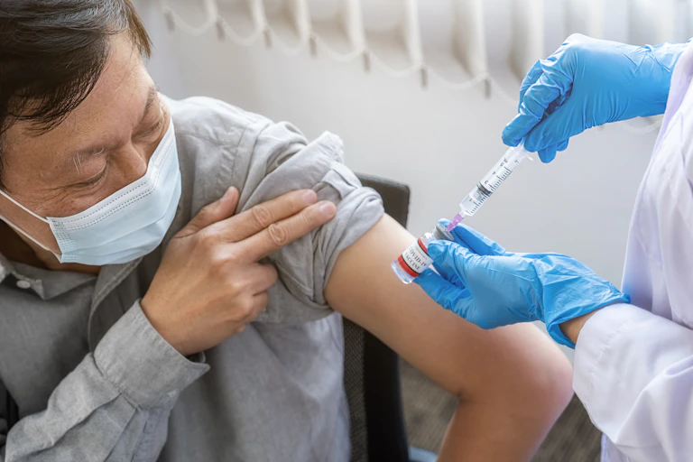 A woman preparing a syringe to vaccinate a man for COVID-19