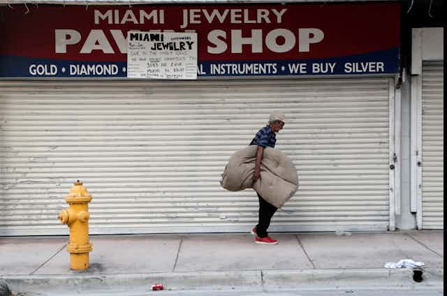 A homeless man carrying his bedding walks past the Miami Jewelry Pawn Shop.