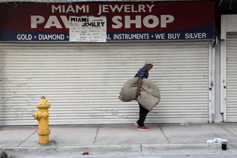 A homeless man carrying his bedding walks past the Miami Jewelry Pawn Shop.
