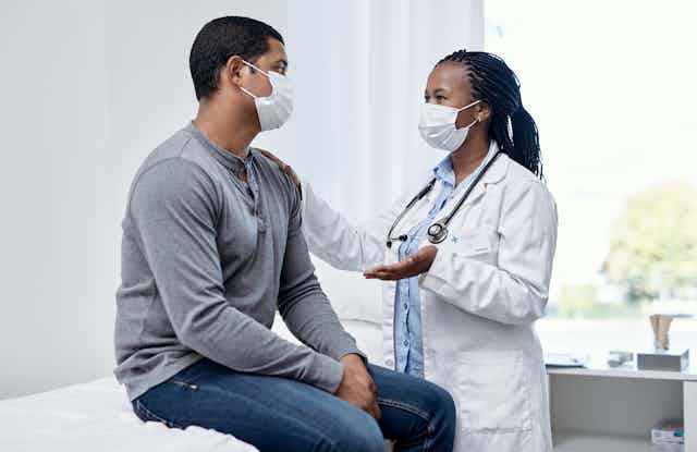 Medical provider wearing face mask speaking to patient wearing face mask in exam room.