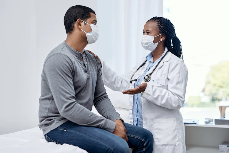 Medical provider wearing face mask speaking to patient wearing face mask in exam room.