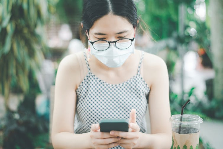 Young woman wearing mask scrolling smartphone sitting outside