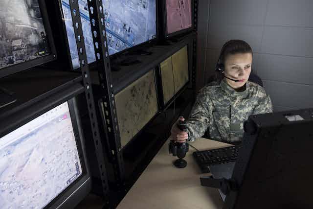 A female drone operator sitting behind a computer with her hand on a joystick