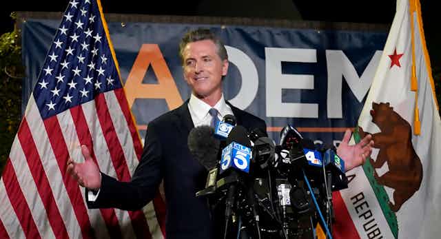 California Governor Gavin Newsom stands in front of an American flag and a Californian flag while speaking to reporters.