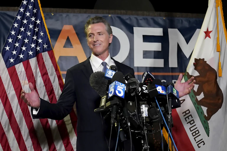 California Governor Gavin Newsom stands in front of an American flag and a Californian flag while speaking to reporters.