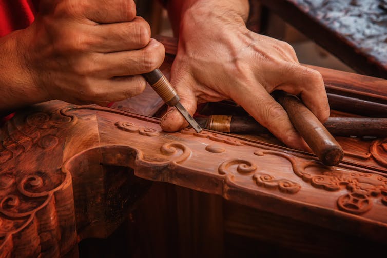 A woodworker chisels patterns into red mahogany.