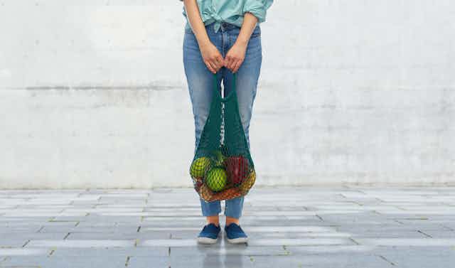 Una persona con una bolsa de la compra con frutas y versuras.