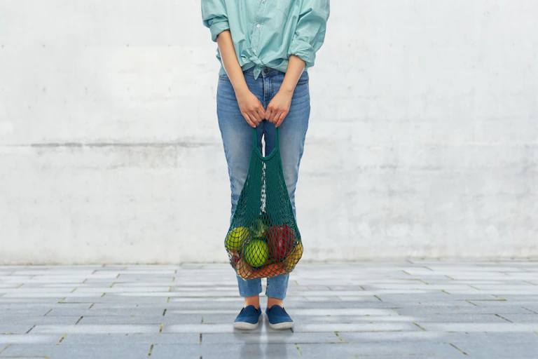 Una persona con una bolsa de la compra con frutas y versuras.