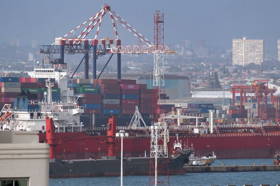 Ships, some loaded with containers, in a port; cranes and city in background