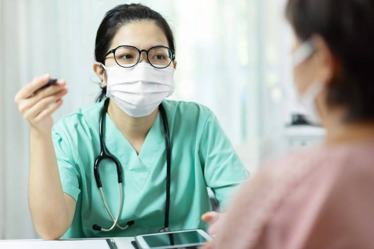 Masked health care provider in green scrubs talking to patient.