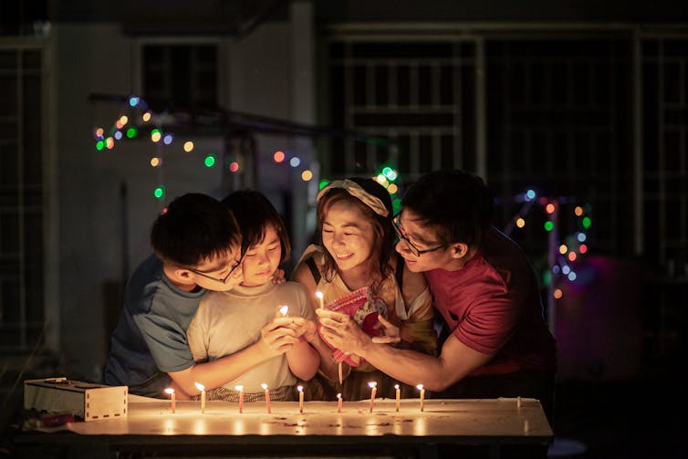 Group of smiling people gathered around lit candles at night.