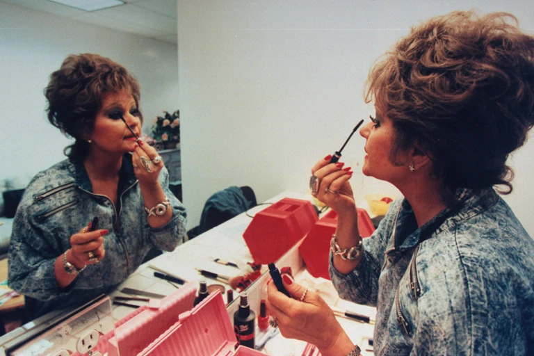 Woman applies eyeliner while looking in the mirror.