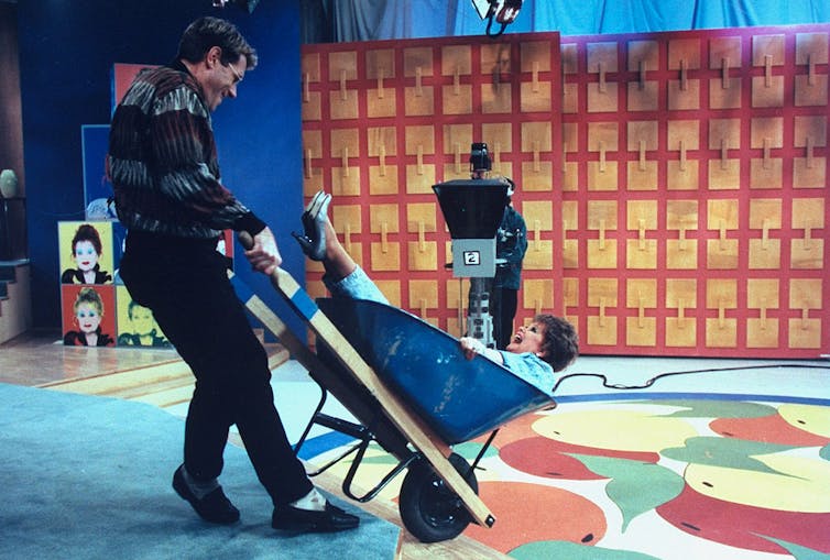 Man pushing a wheelbarrow with a woman in it.