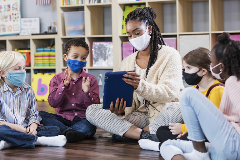 Teacher holding tablet sits between young students