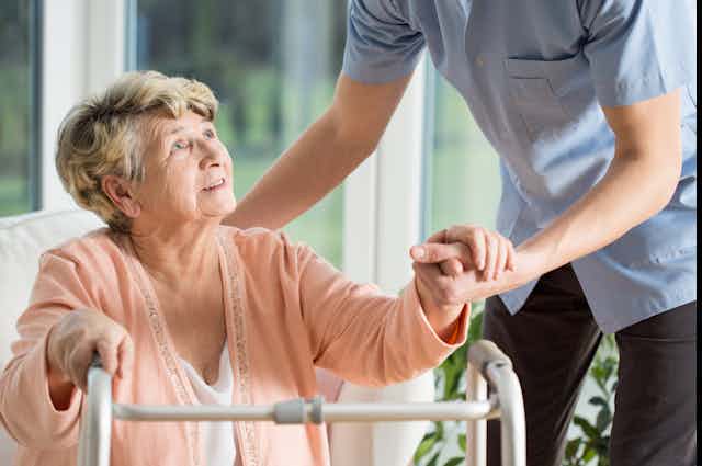older woman with walking frame being helped by nurse