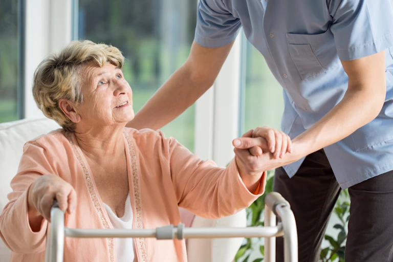 older woman with walking frame being helped by nurse