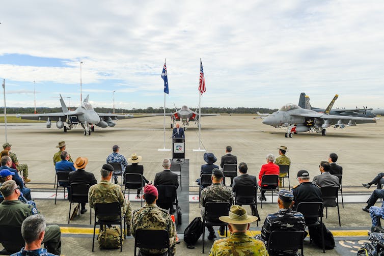 Fighter jets and US and Australian flags in background
of official ceremony on airstrip.