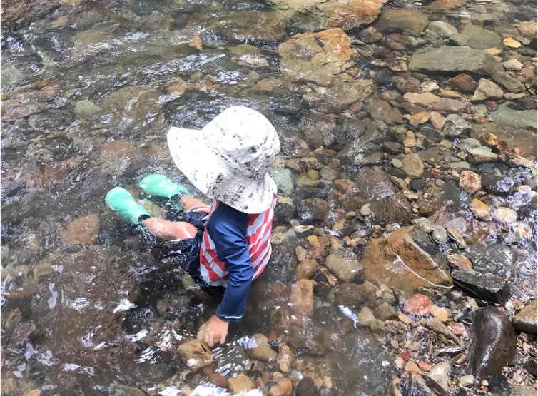 Child sitting in water at the edge of a creek.