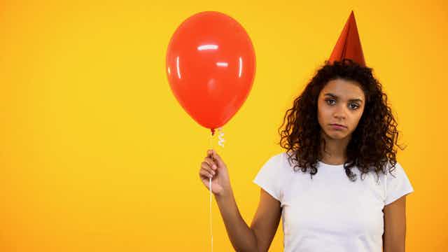 Sad girl in party hat holding balloon.