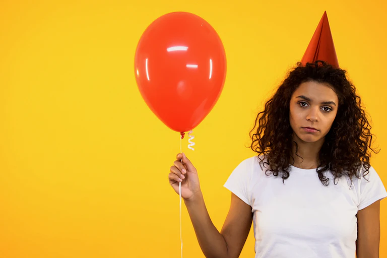 Sad girl in party hat holding balloon.