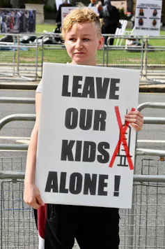 An anti-vaxx protestor in London holds up a poster saying 'Leave our kids alone'.