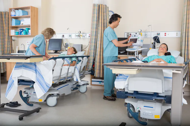 Two nurses are tending to two patients laying in hospital beds.