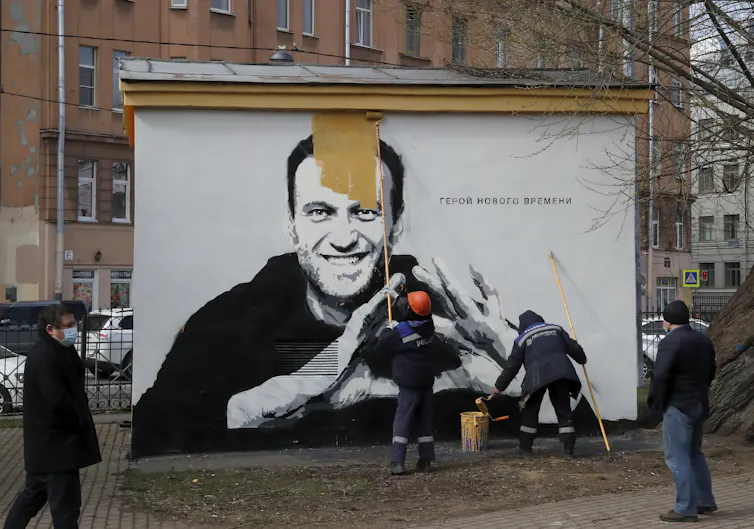 Russian municipal workers paint over a picture of jailed opposition leader Alexei Navalny.