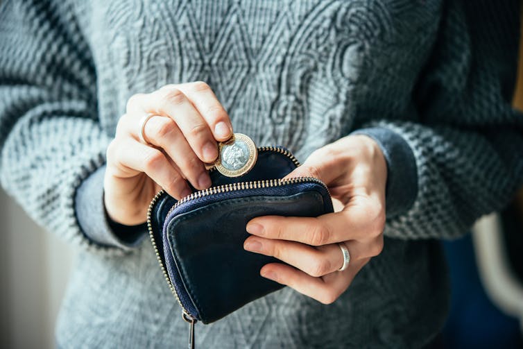 Woman holding an open purse in one hand and a pound coin in the other.